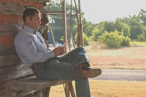 Country man sitting on a rough cut bench on a cell phone.