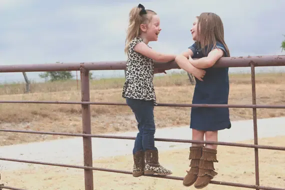 Two young girls laughing on a gate.