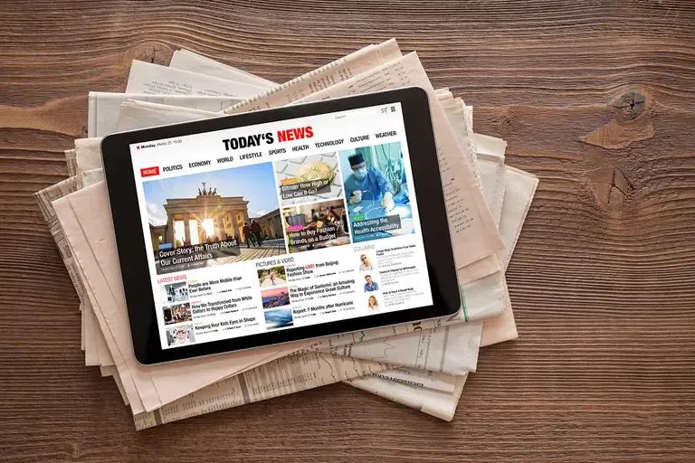 An iPad sitting on top of newspapers showing "Todays News" a page talking about world news.