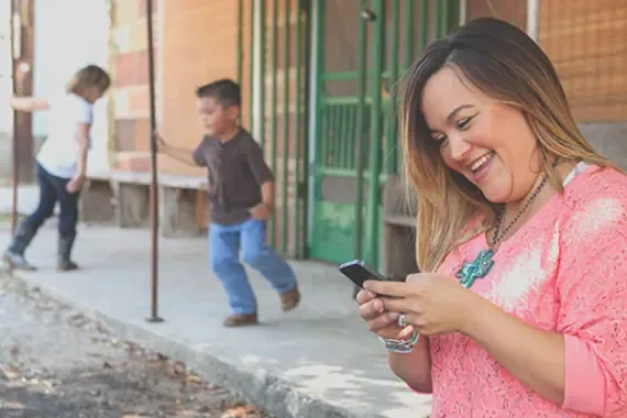 Woman smiling at her phone while children play in the background.