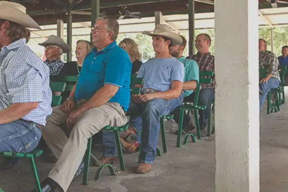 A group of country folk sitting in rows of green benches.